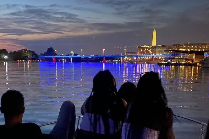 Silhouetted people on a boat with cityscape and monument at dusk.