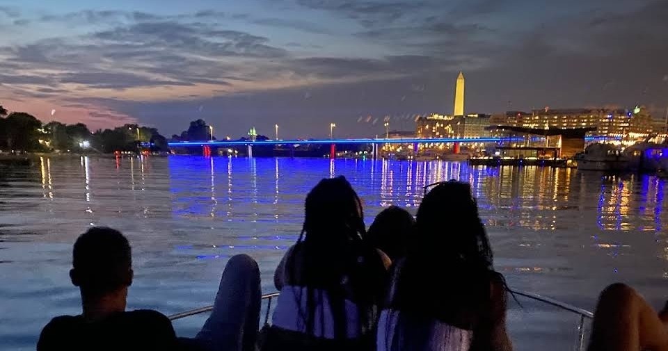 Silhouetted people on a boat with cityscape and monument at dusk.