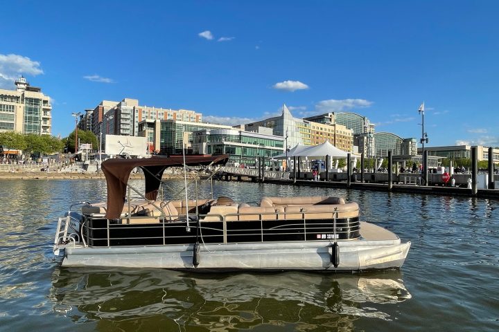 Pontoon boat on water with cityscape and blue sky in background.