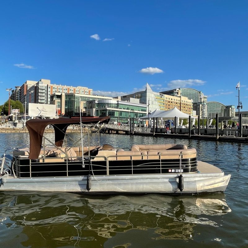 Pontoon boat on water with cityscape and blue sky in background.