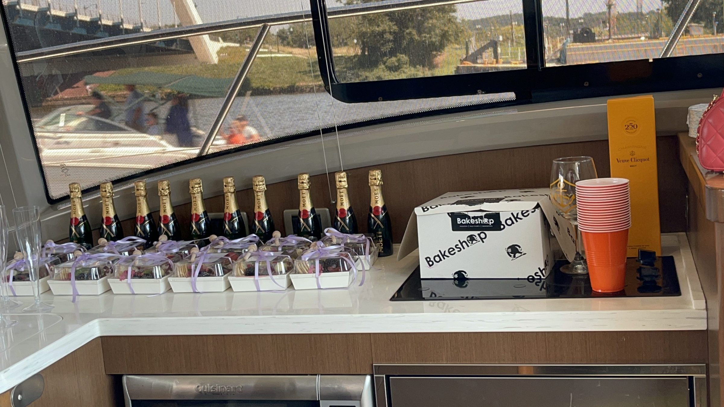 Champagne bottles and dessert boxes arranged on a boat's counter.