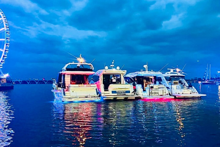 Four yachts moored together at dusk with a Ferris wheel in the background.