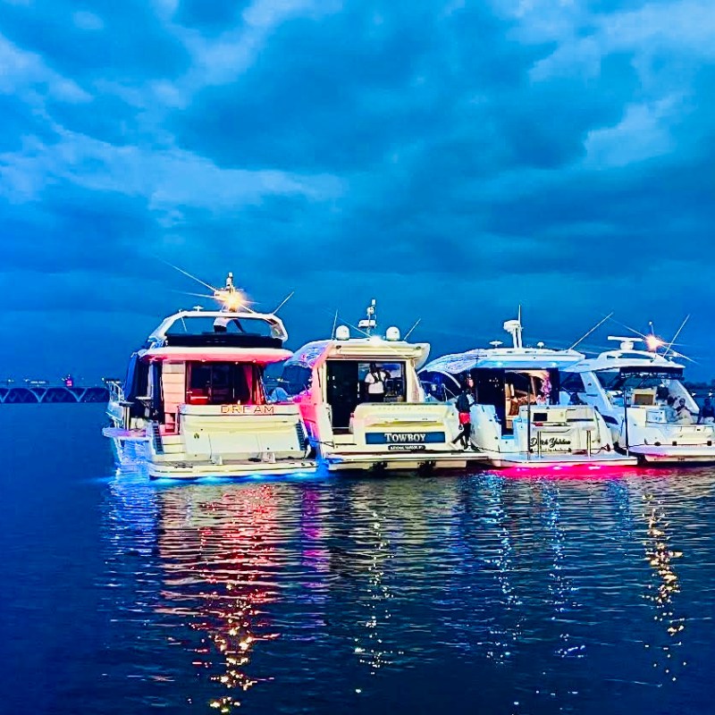 Four yachts moored together at dusk with a Ferris wheel in the background.
