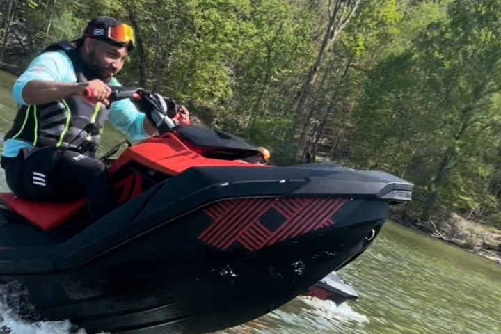 Person riding a red and black jet ski on a lake with trees in the background.