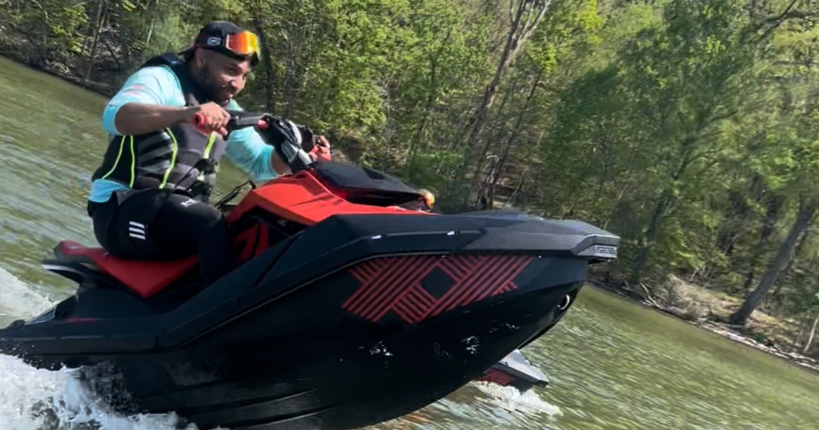 Person riding a red and black jet ski on a lake with trees in the background.
