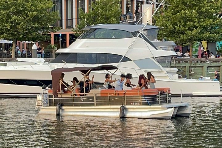 People on a small boat in a city harbor with buildings and trees in the background.