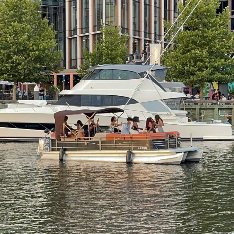 People on a small boat in a city harbor with buildings and trees in the background.