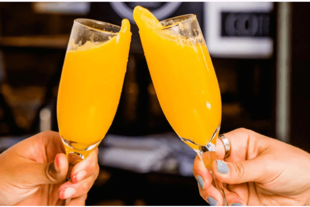 Two hands clinking champagne flutes filled with orange juice.