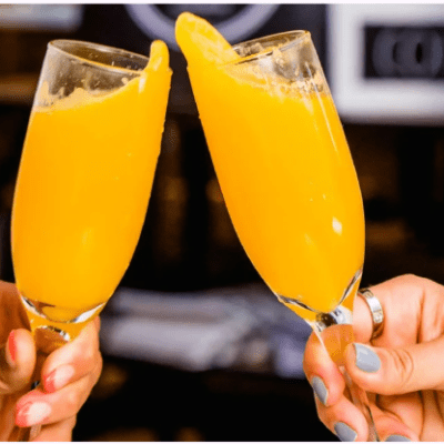 Two hands clinking glasses of orange juice in celebration.