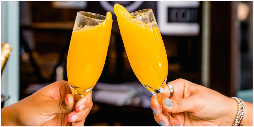 Two hands clinking glasses of orange juice in celebration.