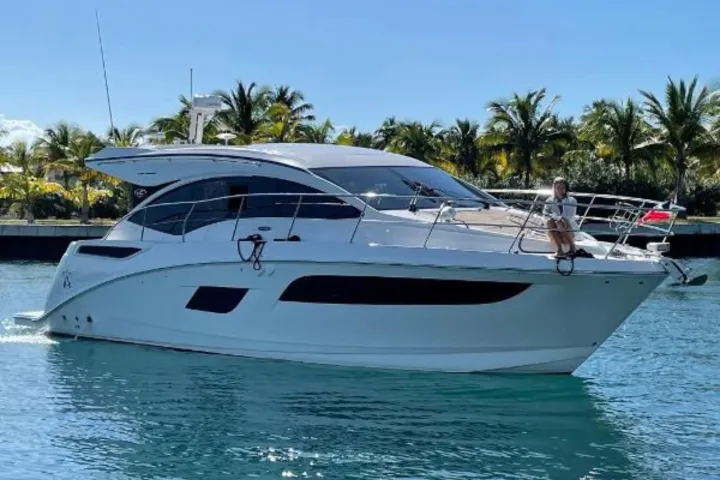 White yacht on blue water with a person sitting on the bow, palm trees in the background.