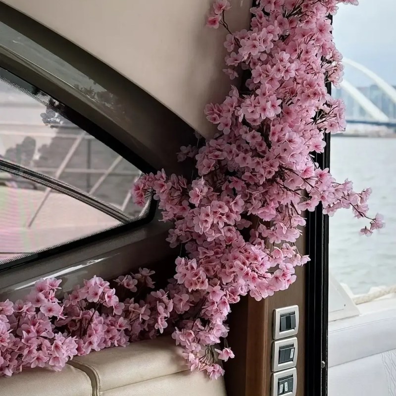 Pink flowers decorate a boat interior with cream seats and window view of water.